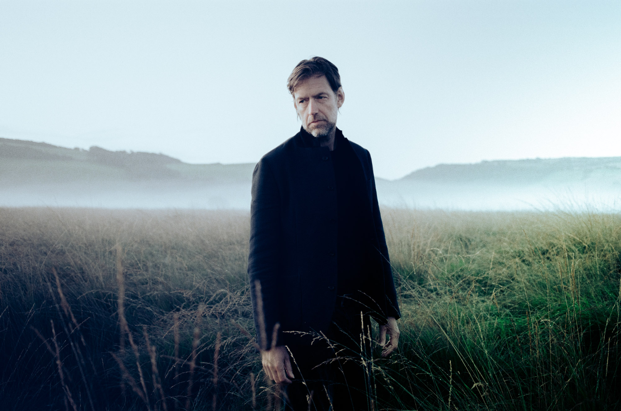 Ed O'Brien, as EOB, standing in a misty field, the portrait his publicists issued for the first single, Brasil, December 2019