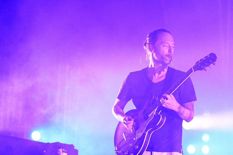 Thom Yorke, hair tied back, playing a hollow-bodied electric guitar in purple stage light with Atoms for Peace at the Melt festival, 21 July 2013